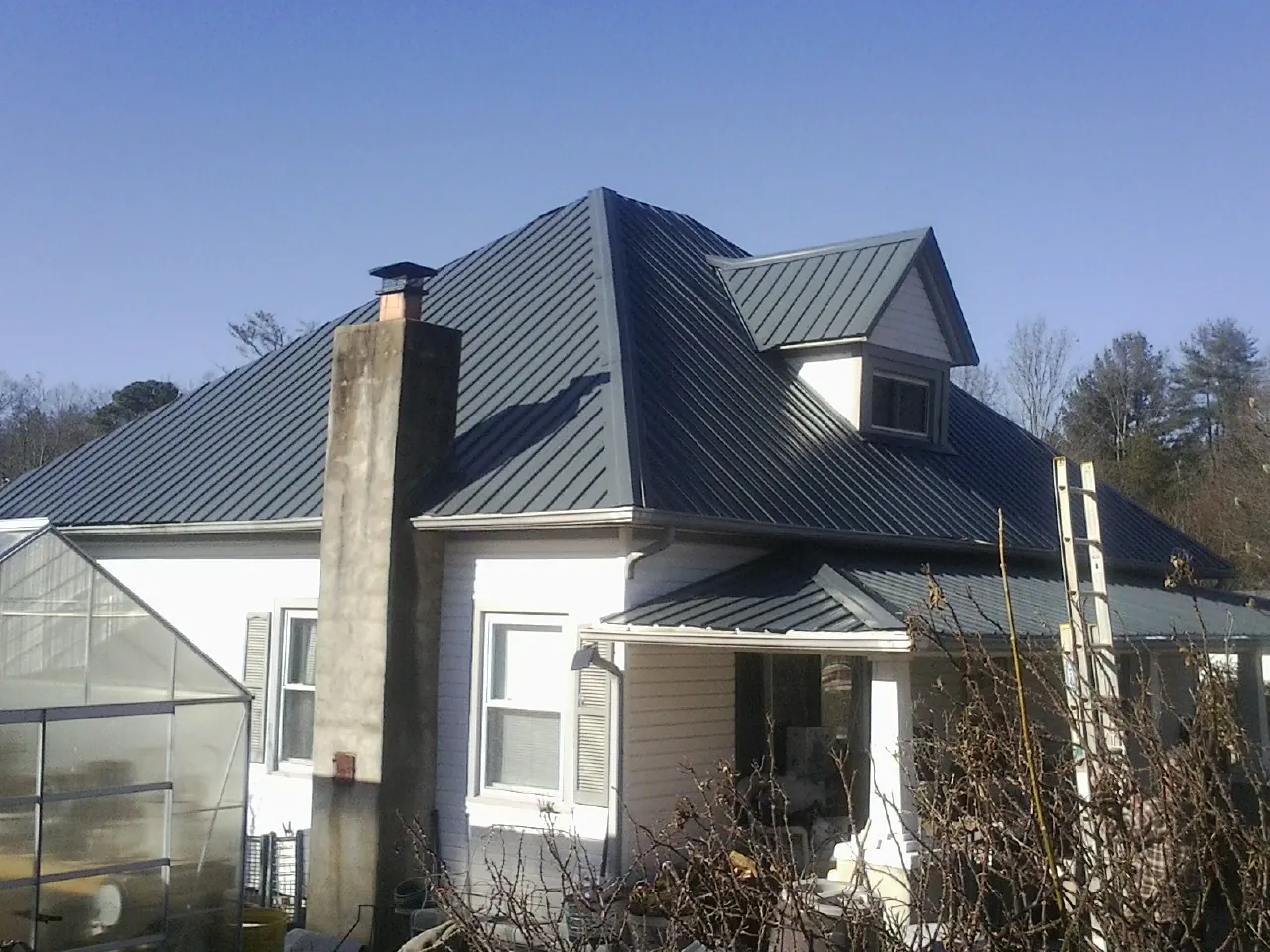 Dark blue standing seam metal roof on a white farmhouse with dormer — Slate & Tile Roof Repair by Roofing Brothers in Brainard