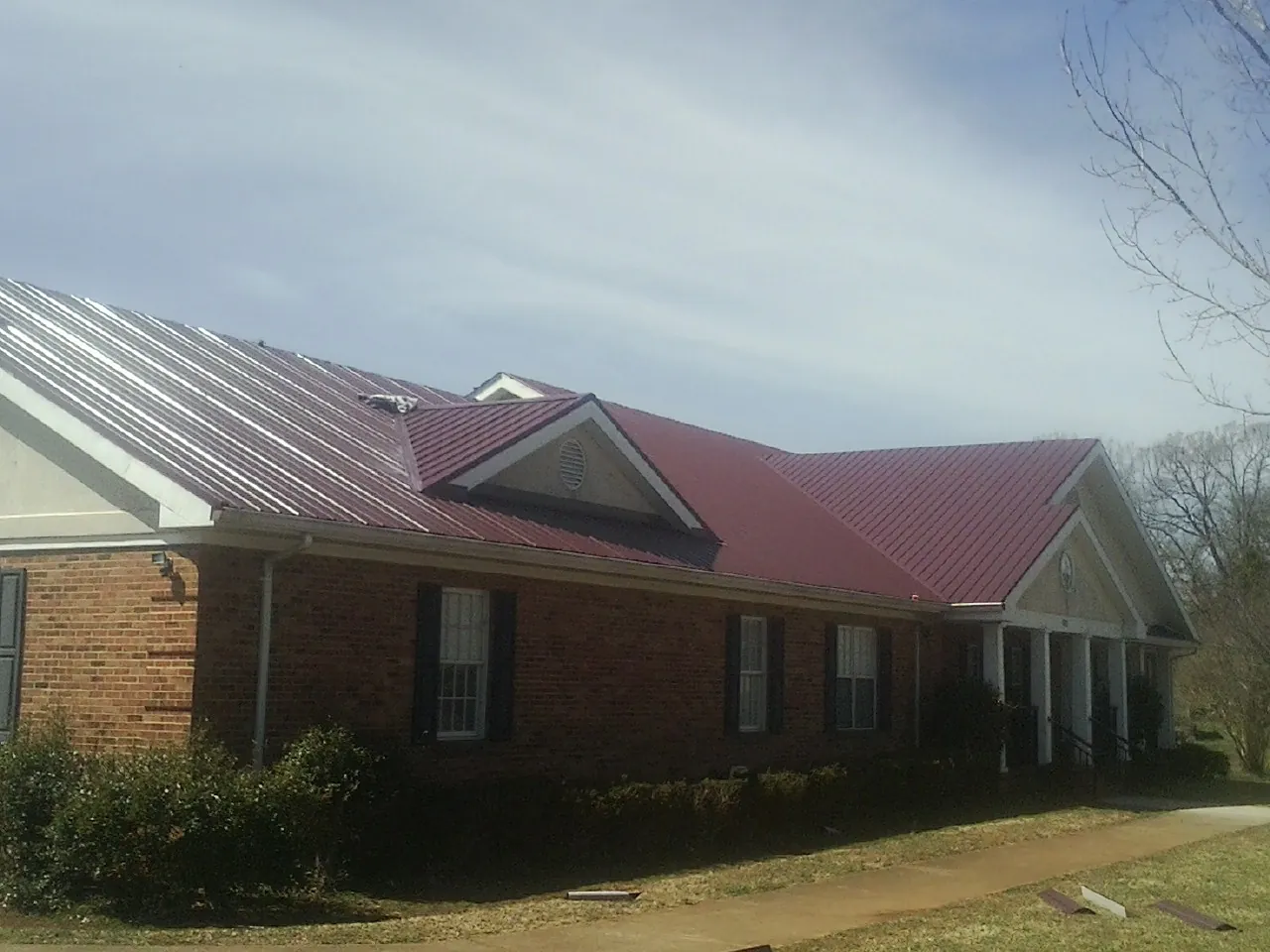 Red metal roof with gabled entries on a long brick building, from a Hail Damage Roof Repair job in Brainard