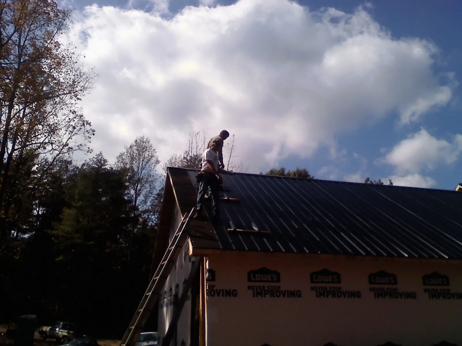 Roofer fastening dark metal panels high against a cloudy sky, from a Roof Inspection job in Brainard