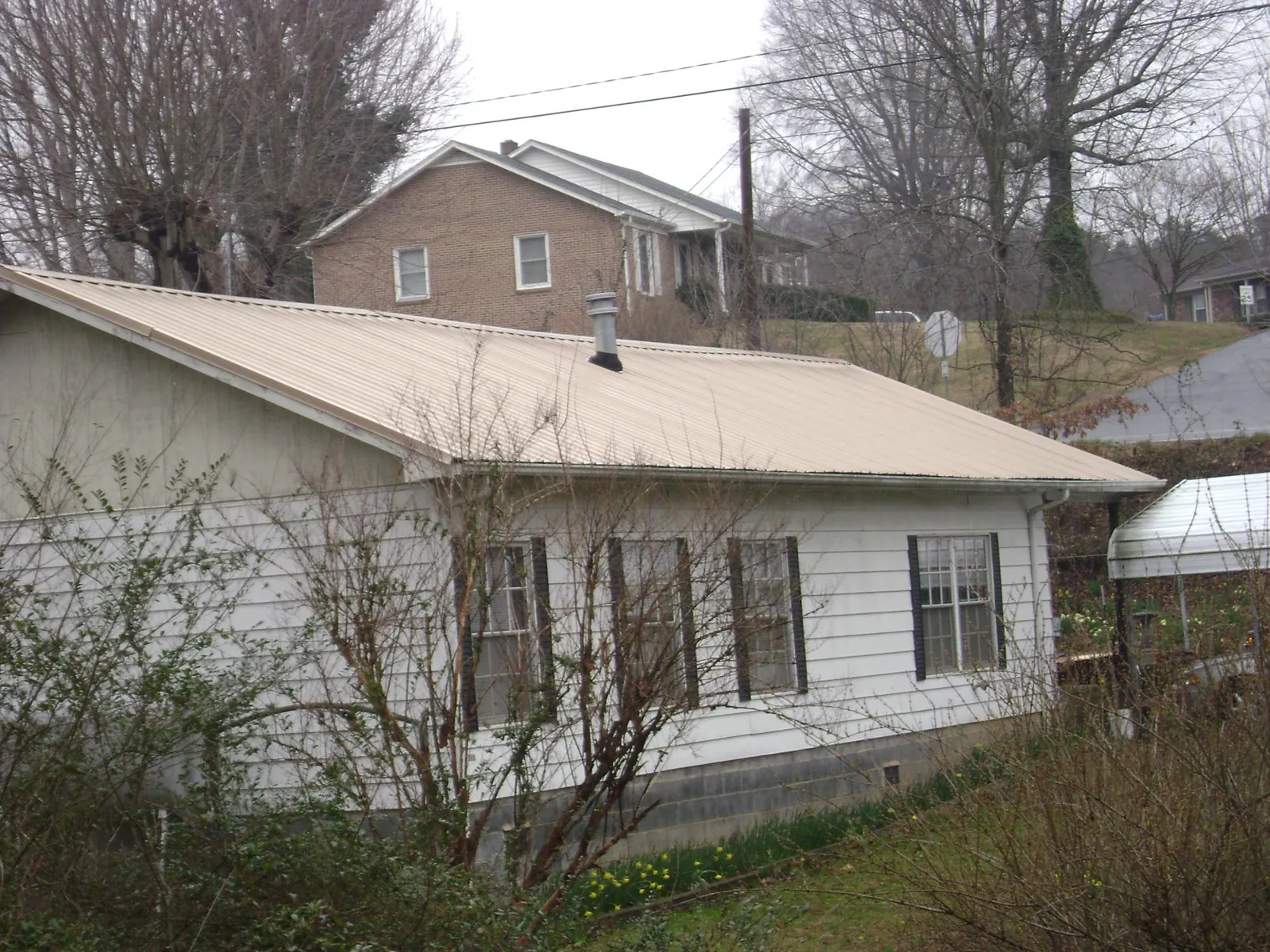Tan metal roof on a white sided house set into a hillside — Commercial Roofing by Roofing Brothers in Brainard